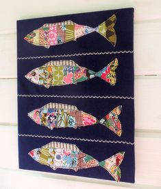 four fish on a wall hanging in front of a white wooden wall with blue background