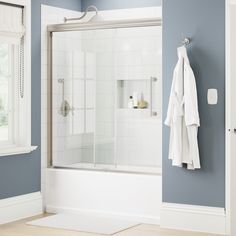 a bathroom with blue walls and white towels hanging on the shower door, next to a window