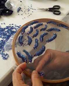 a person is working on something with blue thread and beads in the shape of leaves