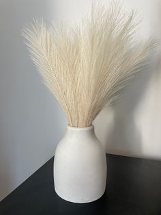 a white vase with some grass in it