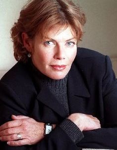 a woman with her arms crossed leaning on a chair and looking at the camera while wearing a black jacket