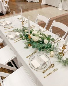 the table is set with white flowers and greenery, gold candlesticks and place settings