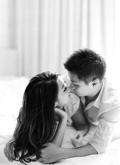 a man and woman laying on top of a bed kissing each other with their noses touching