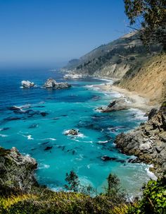 the ocean is blue and green with waves coming in from the rocks on the shore