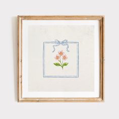 an embroidered picture frame with flowers on it and a blue ribbon around the edge, hanging on a wall