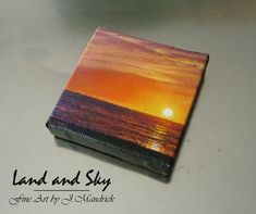 an orange sunset is reflected in the water on a small box that sits on top of a table