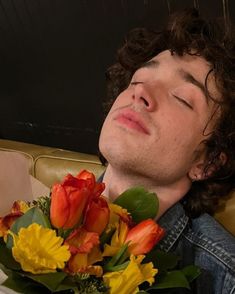 a man laying on a couch with flowers in his lap and eyes closed to the side