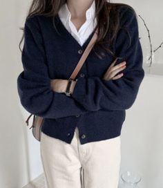 a woman standing with her arms crossed wearing a blue cardigan sweater and white pants