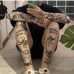 a person sitting on the ground with some tattoos on their arms and legs, holding a cell phone