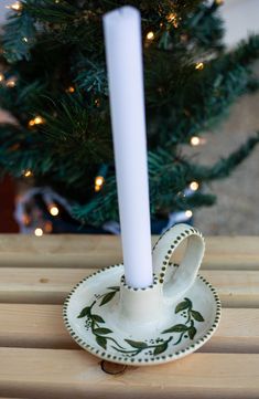 a white candle holder sitting on top of a wooden table next to a christmas tree