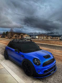 a blue car parked on the side of a road under a dark sky with storm clouds