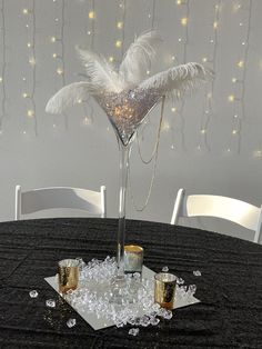 a table topped with glasses and a tall vase filled with white feathers on top of it