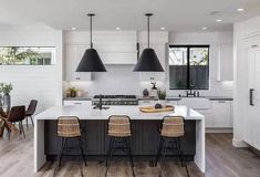 a kitchen with white cabinets and black pendant lights hanging from the ceiling over the island