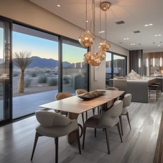 a dining room table with chairs and lights hanging from it's ceiling in front of large windows