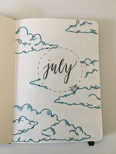 an open notebook with the word july written in cursive writing and clouds on it