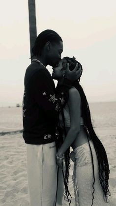 a man and woman kissing on the beach in front of a pole with water behind them