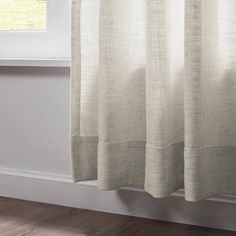 a white curtain hanging from the side of a window in a room with wood floors