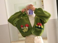 a woman taking a selfie in front of a mirror wearing a green knitted cardigan