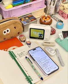 an assortment of school supplies on a desk with a cell phone and other items around it