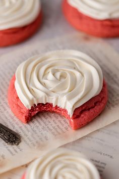 some red velvet cookies with white frosting on top of an open book and a spoon