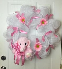 a pink and white wreath with a teddy bear on it, sitting in front of a door