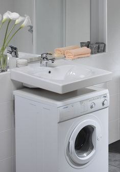 a white washer sitting next to a bathroom sink in front of a mirror with flowers on it