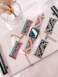 four pieces of jewelry sitting on top of a white table next to a vase with flowers