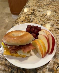 a breakfast sandwich with bacon, cheese and apples on a white plate sitting on a marble counter top