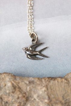 a silver bird necklace sitting on top of a rock