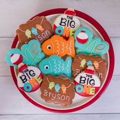 decorated cookies in the shape of fish and letters on a red plate with white wood background