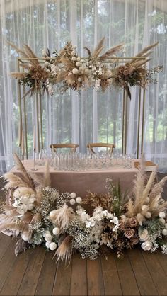 an arrangement of flowers and feathers on a table in front of a window with sheer curtains