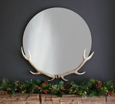 a mirror sitting on top of a mantle covered in christmas greenery and antlers