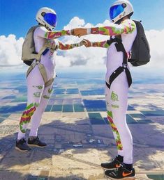 two people standing on top of a building wearing white suits and helmets, one holding the other's hand