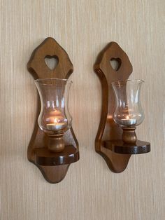 two glass candle holders are mounted on the wall next to each other with wood accents