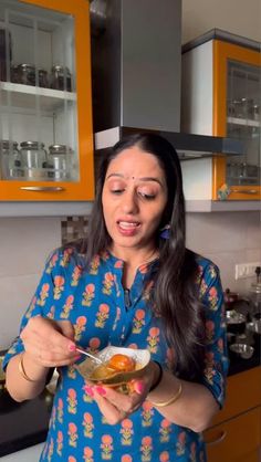 a woman in a blue dress is holding a spoon and looking at the food she has on her plate