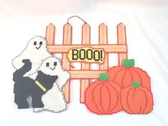 two cross stitch halloween decorations on a white tablecloth, one with a ghost and the other with pumpkins