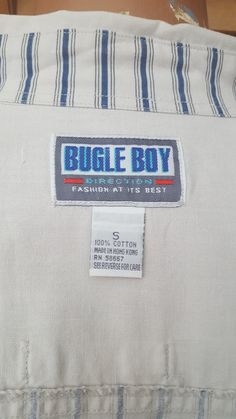 "This is a hip, vintage 1990s, 100% cotton casual shirt by Bugle Boy, made in Hong Kong The long-sleeved shirt has two front flapped pockets, one heavily embellished with applique and embroidery declaring \"Challenge Bugle Boy Clothing - Enjoy - The Right Look!\" The shirt is a navy and beige ticking stripe, with the collar, shoulders, back yoke, and pocket flaps being solid beige. There is an oversized \"locker loop\" on the back yoke. The shirt is marked a size Small, but being a \"big shirt\" 90s Cotton Collared Shirt, 90s Style Cotton Collared Shirt, 90s Style Cotton Button-up Shirt, Solid Beige, Work Coat, Big Shirt, Boy Clothing, Chattanooga Tn, Ticking Stripe