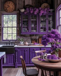 a kitchen with purple cabinets and flowers on the counter top, along with a wooden dining table