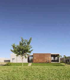 the house is made out of concrete and has grass on both sides, with a tree in the foreground