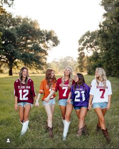 four girls in football jerseys are walking through the grass with one girl holding her hand on her hip