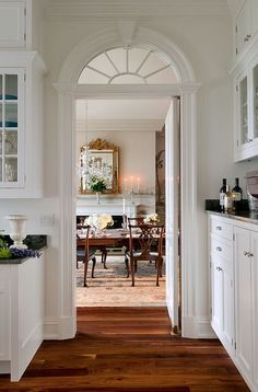 an archway leading to a dining room and kitchen area with white cabinets, wood floors and hardwood flooring