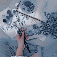 a person sitting on the floor with paint and brushes in their hands, surrounded by art supplies