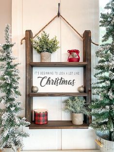 a shelf with christmas decorations on it in front of two trees and a sign that says, its beginning to look like christmas