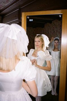 a woman in a white wedding dress looking at herself in the mirror with her veil pulled back