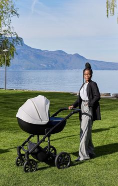 a woman standing next to a baby stroller in the grass with mountains in the background