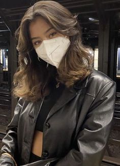 a woman wearing a face mask while sitting on a subway train platform with her hands in her pockets