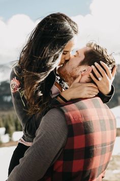 a man and woman kissing each other while standing in front of snow covered mountain range