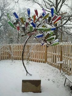 a tree that has been made out of wine bottles is in the snow near a fence