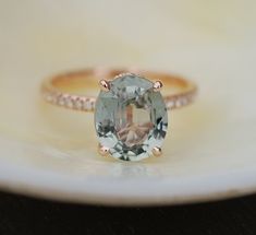 an oval cut green amethyst sits on top of a white plate with a gold band