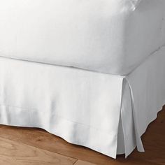 a white bed skirt with pleated edges on a wooden floor in front of a window